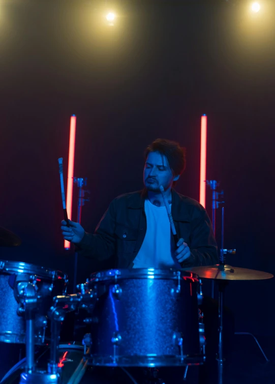 a man that is sitting in front of a drum set, holding a blue lightsaber, profile image, b - roll, ignant