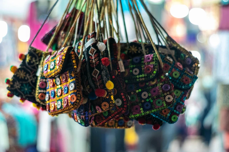 a bunch of purses hanging from a ceiling, a cross stitch, trending on unsplash, on an indian street, avatar image, bedazzled, pouches