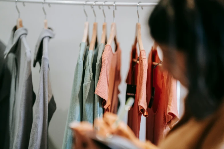 a woman standing in front of a rack of clothes, by Carey Morris, trending on pexels, gray and orange colours, inspect in inventory image, green and brown clothes, wearing an orange t shirt