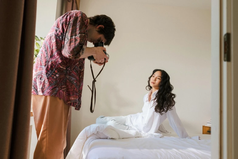 a woman sitting on top of a bed next to a man, pexels contest winner, shooting, wearing robe, brunette, making of