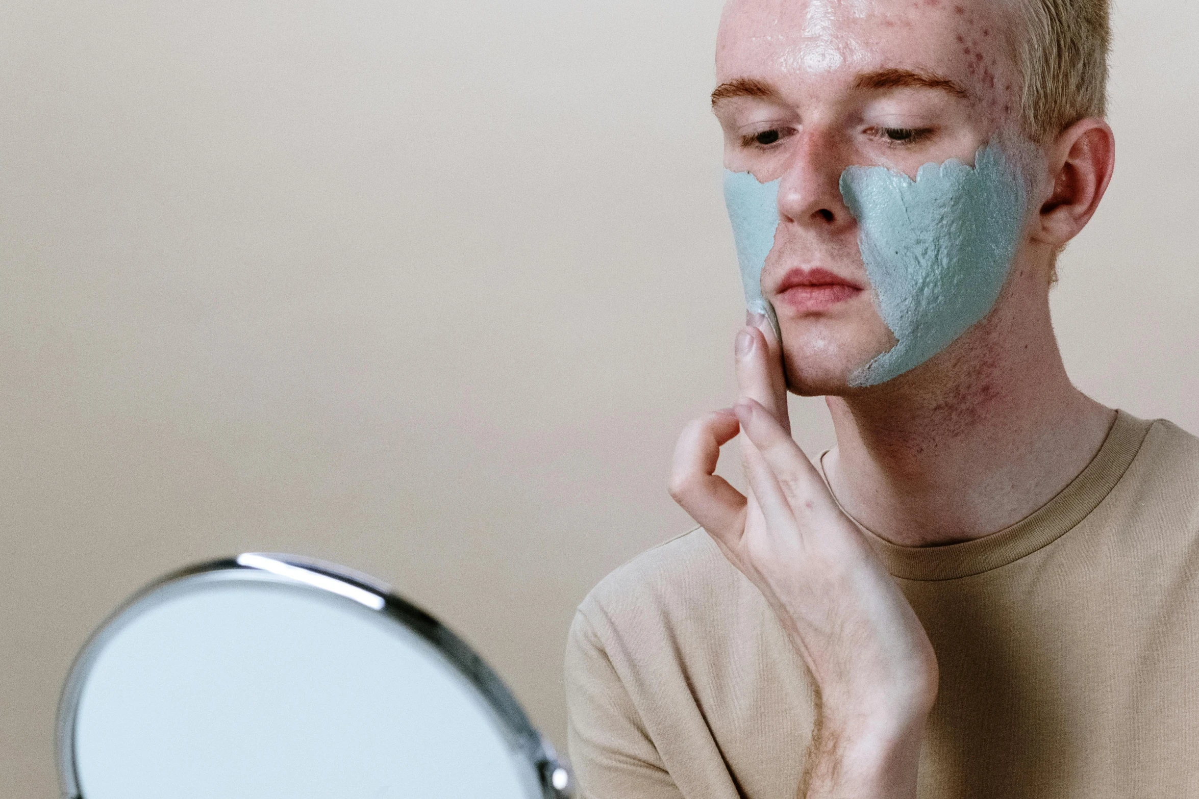 a man with a blue face mask in front of a mirror, trending on pexels, freckled pale skin, skin painted with green, photoshoot for skincare brand, pearlescent skin