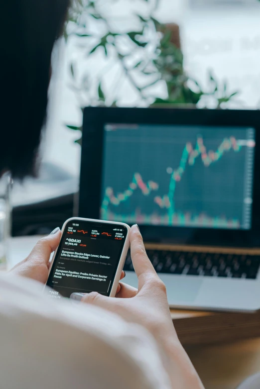 a person sitting in front of a laptop and a cell phone, displaying stock charts, wētā fx, thumbnail, square