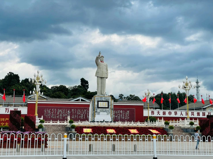 a large statue of a man standing in front of a building, a statue, inspired by Zhang Shunzi, white buildings with red roofs, mao zedong, avatar image