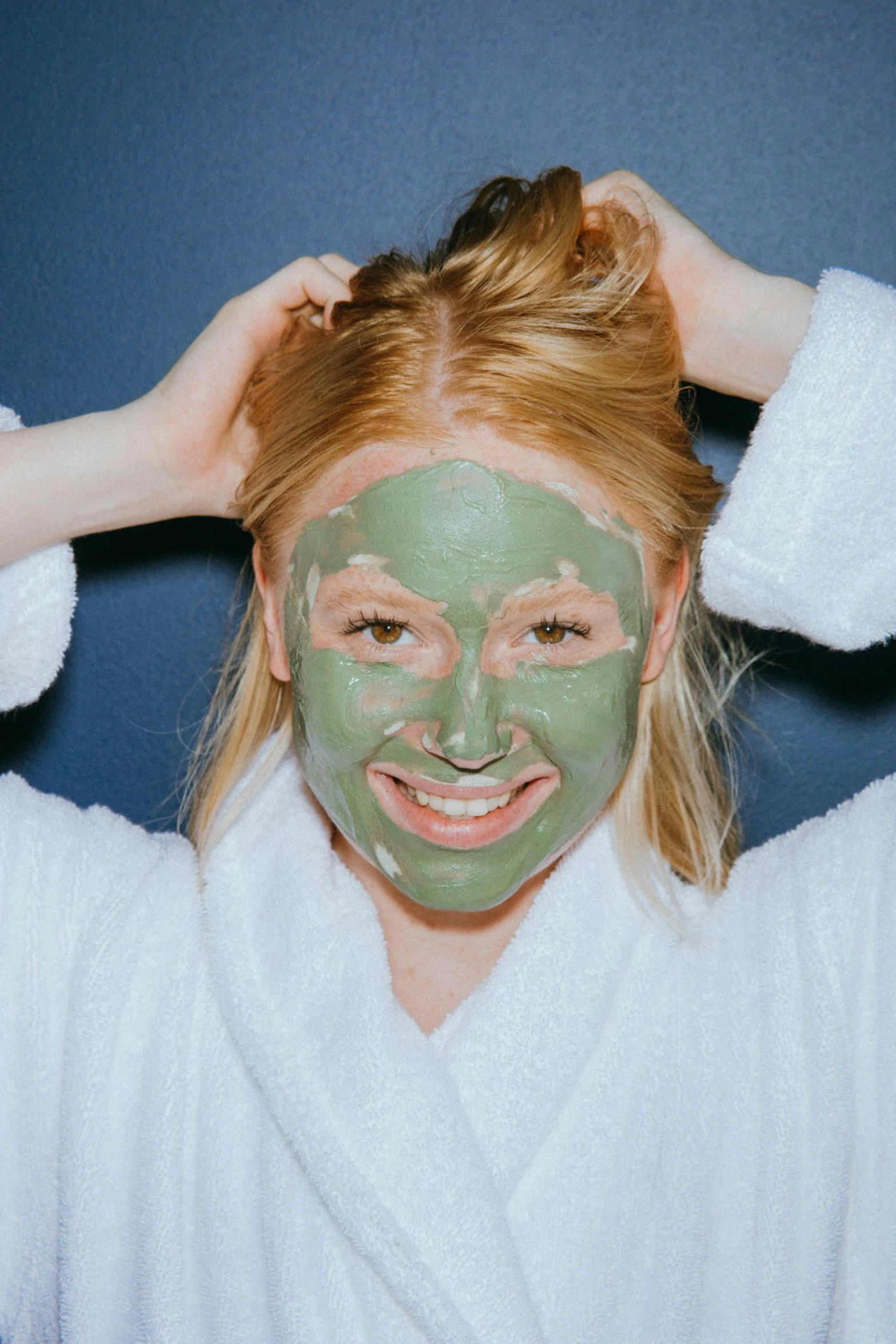 a woman putting a facial mask on her face, a colorized photo, trending on pexels, green robe, happily smiling at the camera, ivy's, bedhead