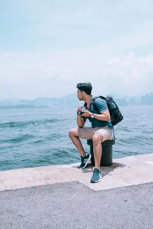 a man sitting on a bench next to the water, pexels contest winner, happening, a backpack, in hong kong, profile posing, 🚿🗝📝