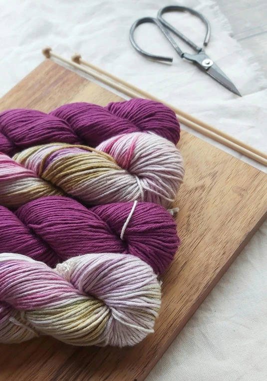 two skeins of yarn and a pair of scissors on a cutting board, inspired by Violet Oakley, unsplash, process art, 2 5 6 colours, beauteous sumptuous, wine, rosen zulu