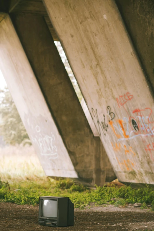 a tv sitting under a bridge with graffiti on it, inspired by Elsa Bleda, unsplash, graffiti, fallen columns, bunkers, portrait closeup, wide film still