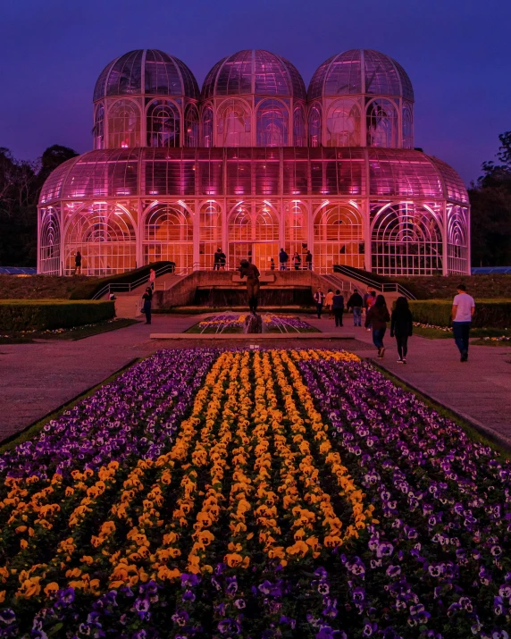 a group of people walking around a flower garden, by Alejandro Obregón, pexels contest winner, art nouveau, tall windows lit up, pink and orange colors, a crystal palace, greenhouse in the background