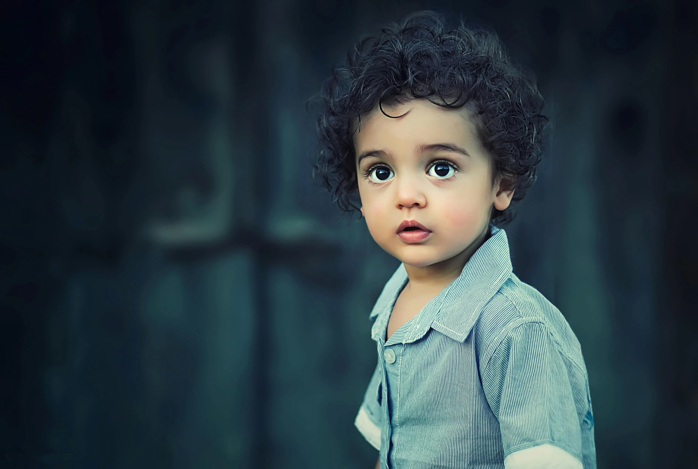 a little boy standing in front of a wooden door, by Lucia Peka, art photography, curly middle part haircut, paul barson, closeup of an adorable, desaturated blue