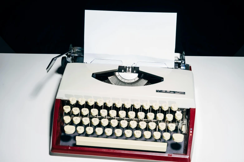 a red and white typewriter sitting on top of a table, lit from above, 1 9 7 0 s, getty images, platon