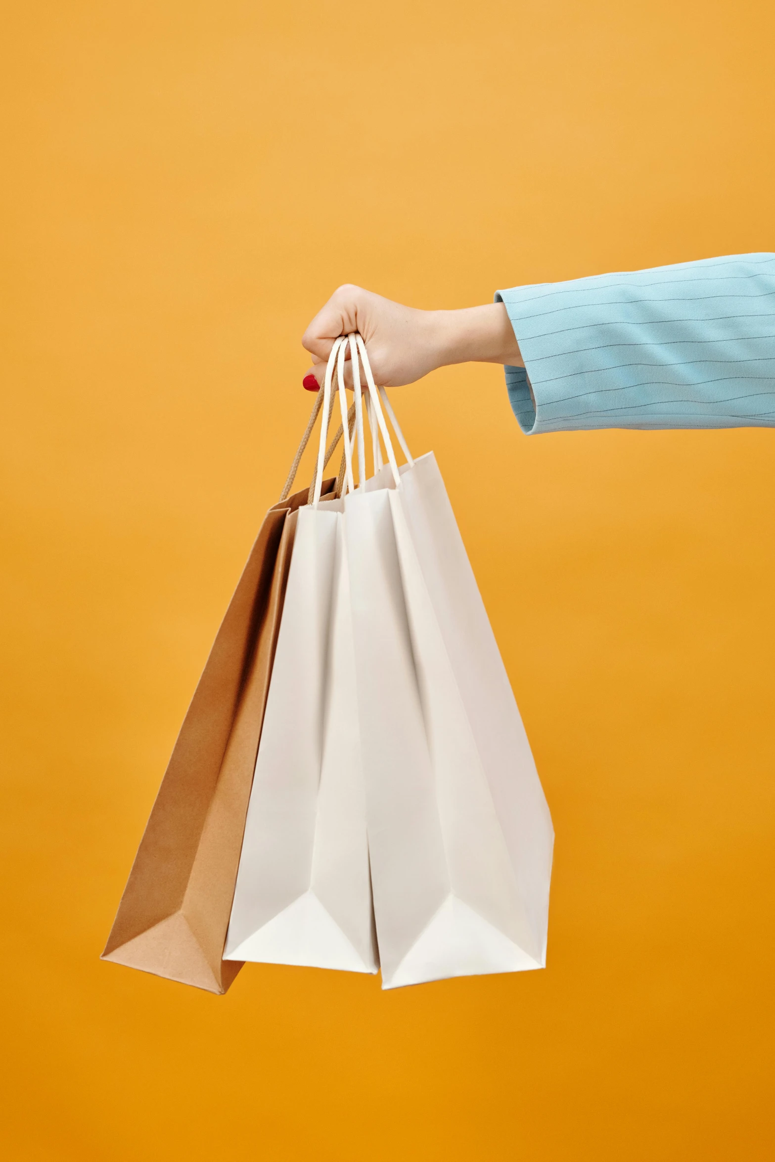 a woman's hand holding shopping bags against an orange background, happening, arper's bazaar, fan favorite, brown paper, white clothing