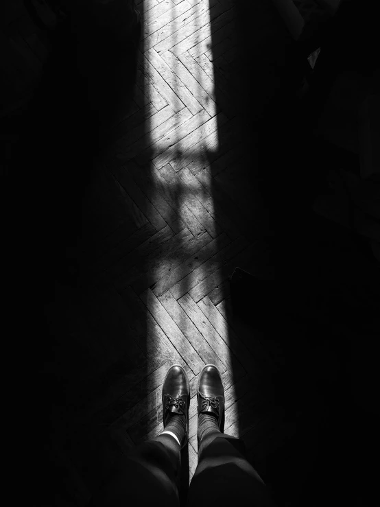 a black and white photo of a person standing in front of a window, by Lucia Peka, unsplash, light and space, black shoes, spotlight from above, shot on iphone 6, in church