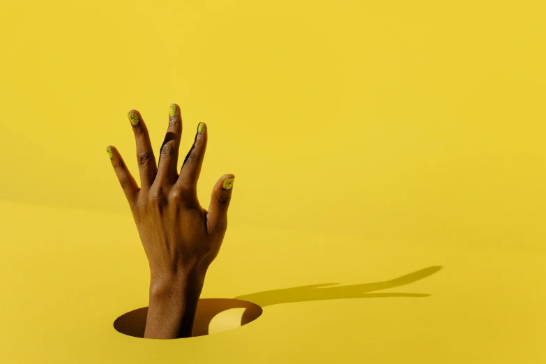 a person's hand sticking out of a hole, an album cover, inspired by Lucio Fontana, trending on pexels, hyperrealism, yellow makeup, ( ( dark skin ) ), aida muluneh, gradient yellow