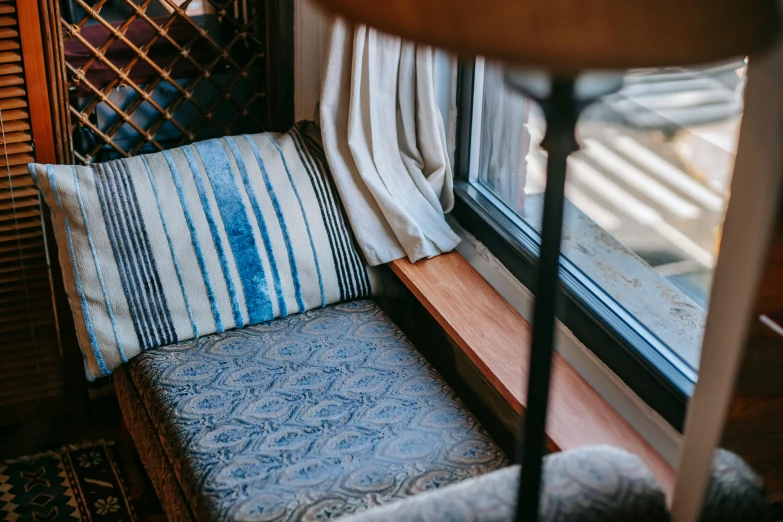 a chair sitting in front of a window next to a lamp, inspired by Marià Fortuny, unsplash, arts and crafts movement, winter blue drapery, striped, asleep, balcony
