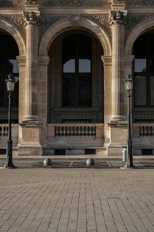 a person sitting on a bench in front of a building, inspired by Albert Guillaume, pexels contest winner, lamps on ground, musee d'orsay 8 k, sparse detail, archs and columns