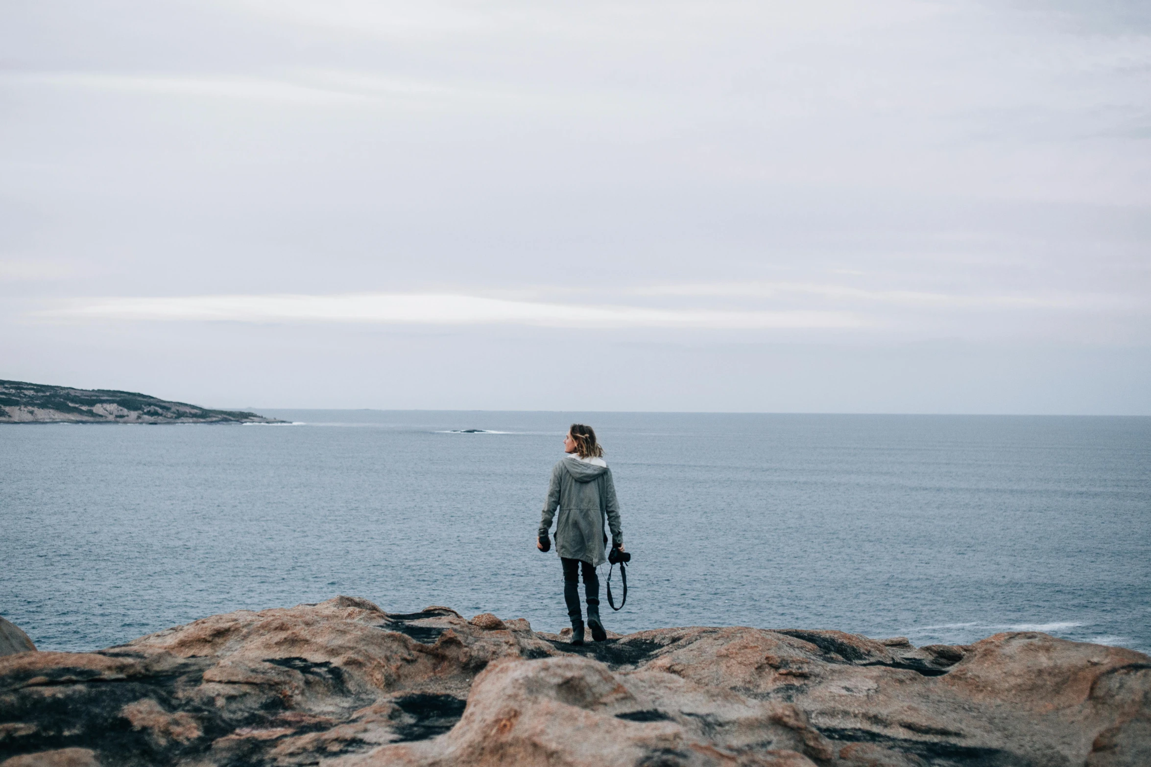 a person standing on a rock in front of the ocean, by Christen Dalsgaard, pexels contest winner, grey, casually dressed, looking onto the horizon, lachlan bailey