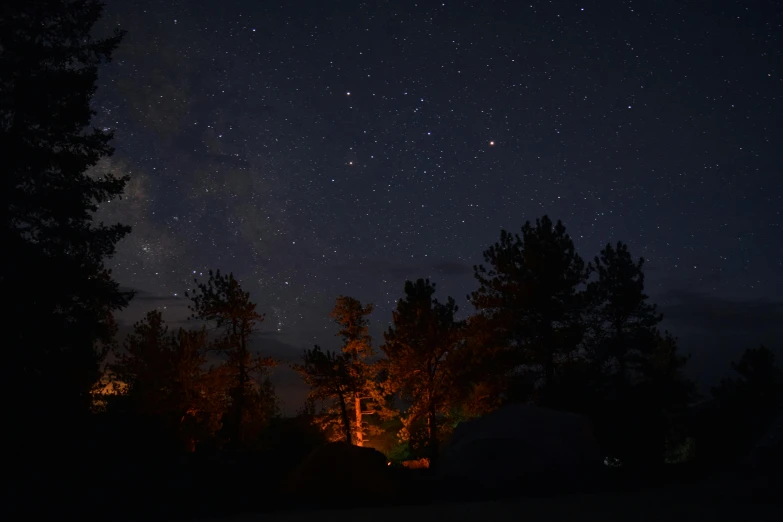 a camper is lit up at night under the stars, a picture, dark pine trees, cinematic shot ar 9:16 -n 6 -g, planets in the sky, red cloud light