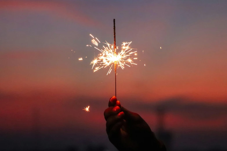 a person holding a sparkler in their hand, pexels, at sunset, fireworks in the background, instagram post, background image