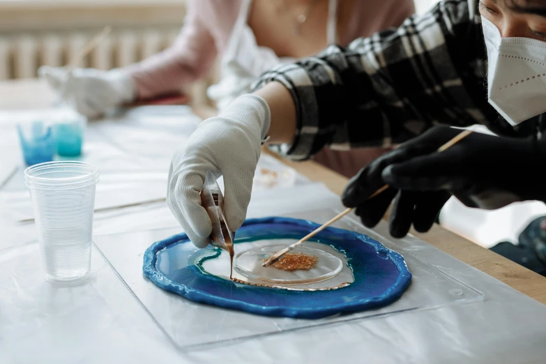 a group of people sitting at a table with a plate of food, a hyperrealistic painting, trending on pexels, process art, epoxy resin, rendering a blue rose, painting on a badge, aboriginal art