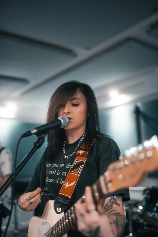 a woman playing a guitar and singing into a microphone, an album cover, by Robbie Trevino, trending on unsplash, panoramic, instagram story, low quality photo, looking serious