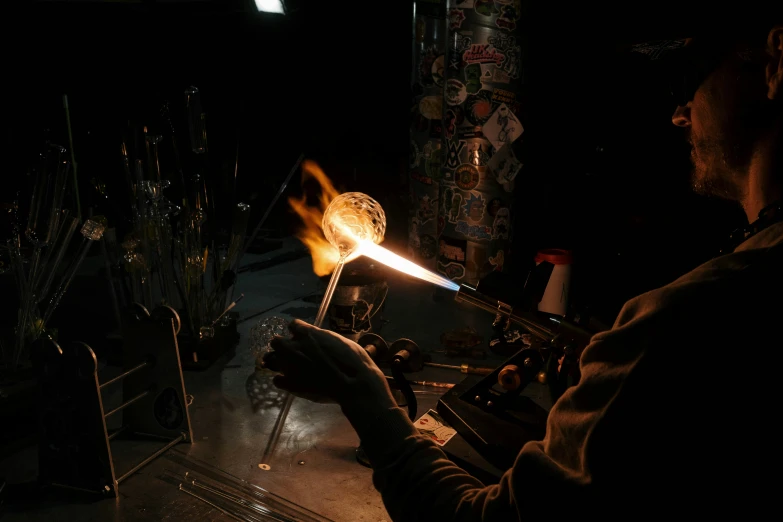 a man that is standing in front of a fire, glassware, at night, smoking soldering iron, during the night
