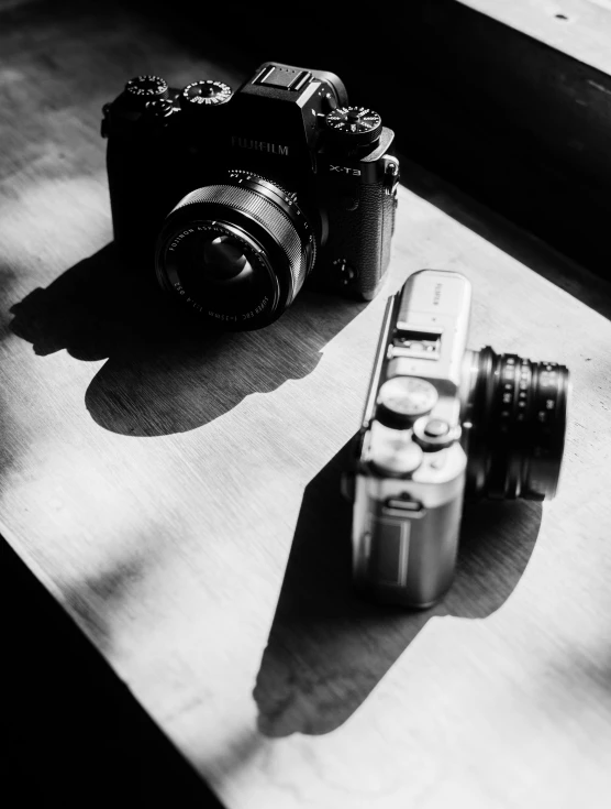 a couple of cameras sitting on top of a wooden table, by Zoltán Joó, cinematic. by leng jun, light and shadow, by greg rutkowski, b&w photograph