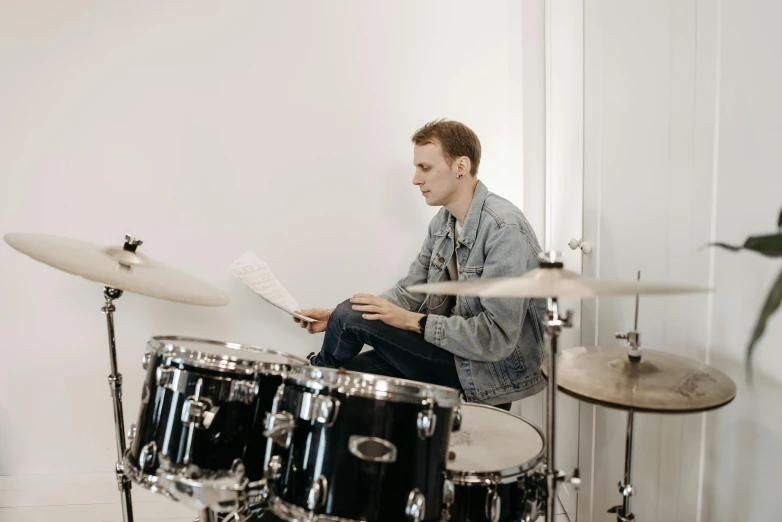 a man sitting in front of a drum set, in a white room, sheet music, best practice, on a pale background