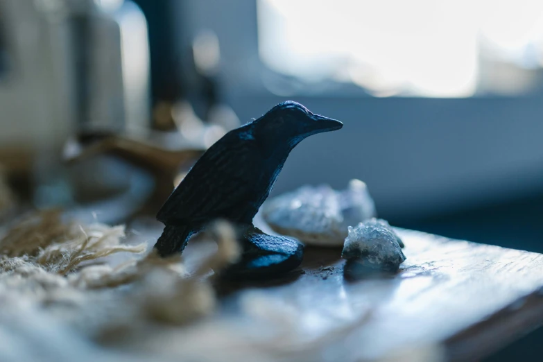a black bird sitting on top of a wooden table, a surrealist sculpture, inspired by Leonora Carrington, unsplash contest winner, magical realism, carved from sapphire stone, witchy, miniature product photo, natural morning light