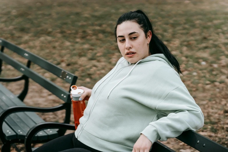 a woman sitting on a bench with a drink in her hand, inspired by Ion Andreescu, trending on pexels, happening, fat belly, wearing a tracksuit, sydney park, heavy looking