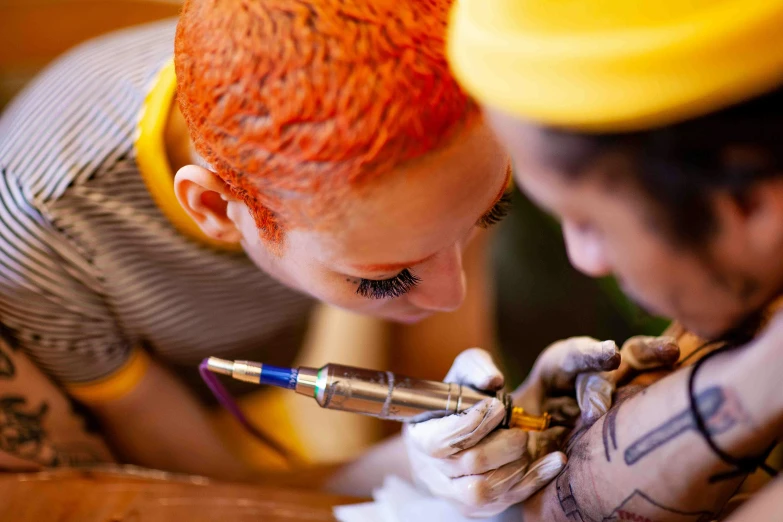a woman getting a tattoo on another woman's arm, a tattoo, by Julia Pishtar, pexels, process art, bright orange hair, sailor jerry tattoo flash, 🦩🪐🐞👩🏻🦳, face paint