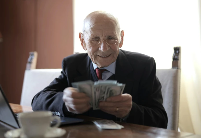 a man sitting at a table with money in front of him, a portrait, by Jesper Knudsen, pexels contest winner, grandfatherly, a still of a happy, 15081959 21121991 01012000 4k, commercial