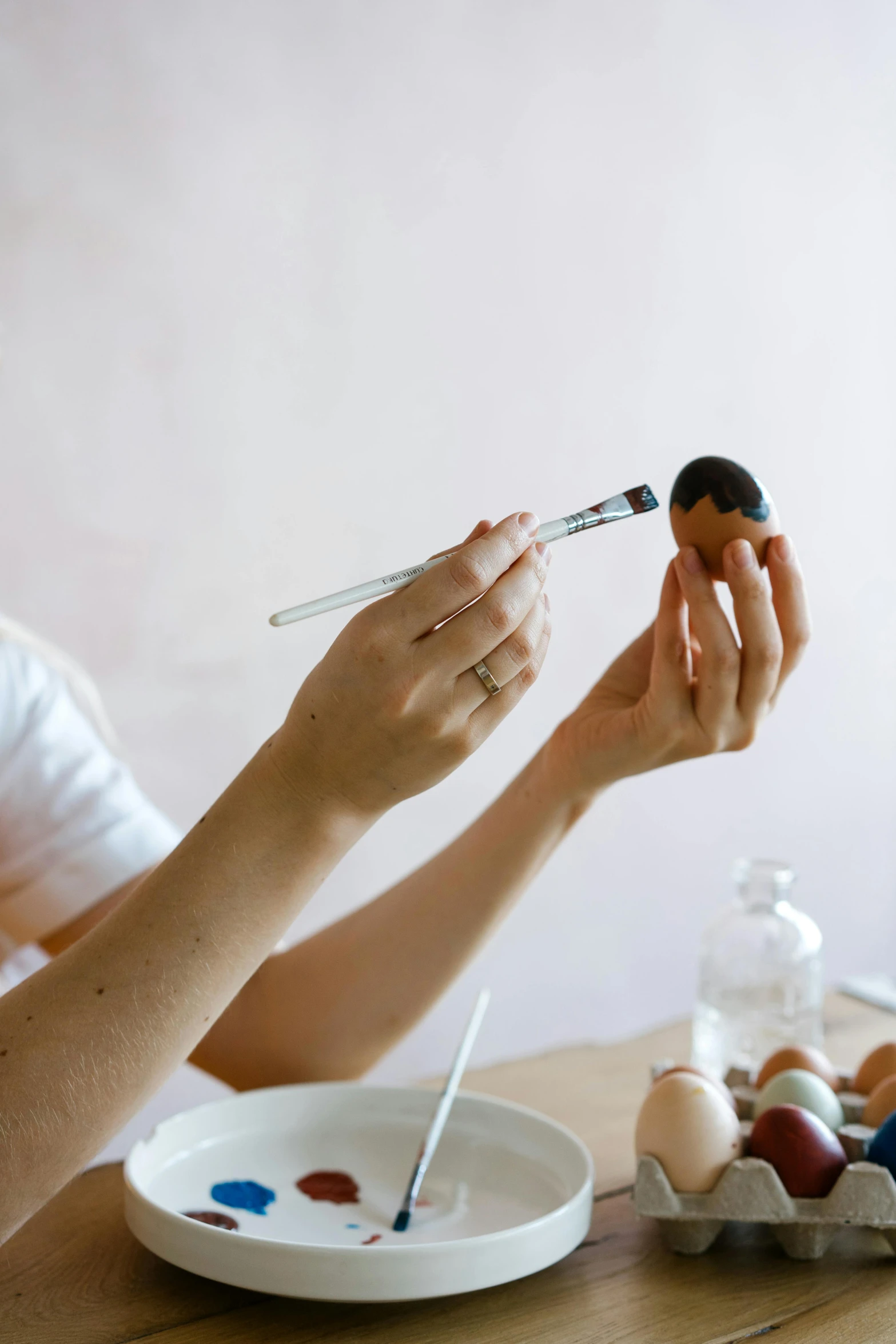 a woman sitting at a table painting eggs, a photorealistic painting, by Julia Pishtar, unsplash, holding brush, line sleek, studio product shot, black paint