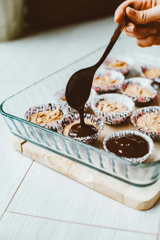 a person scooping a spoon into a tray of cupcakes, by Lucette Barker, chocolate sauce, thumbnail, cooking, crackles