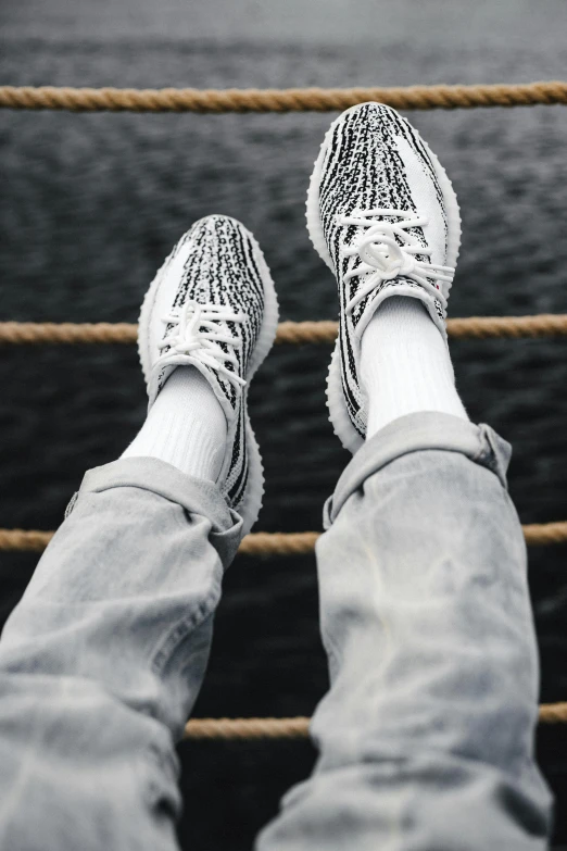 a person's feet on a rope with a body of water in the background, trending on unsplash, yeezy collection, white metallic, on ship, white with black spots