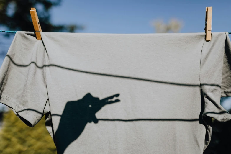a t - shirt hanging on a clothes line with a shadow of a dog on it, inspired by Storm Thorgerson, unsplash, dirty linen robes, people's silhouettes close up, outdoor photo, shadows screaming