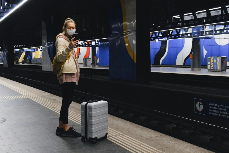 a woman standing at a train station with a suitcase, by Carey Morris, pexels contest winner, graffiti, people are wearing masks, technology, australian, rectangle