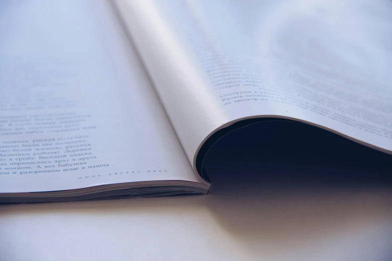 an open book sitting on top of a table, magazine photograph, white paper, curved, close up photograph