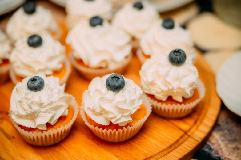 a wooden plate topped with cupcakes covered in frosting, by Adam Marczyński, pexels, renaissance, blueberries, essence, cream, puffy