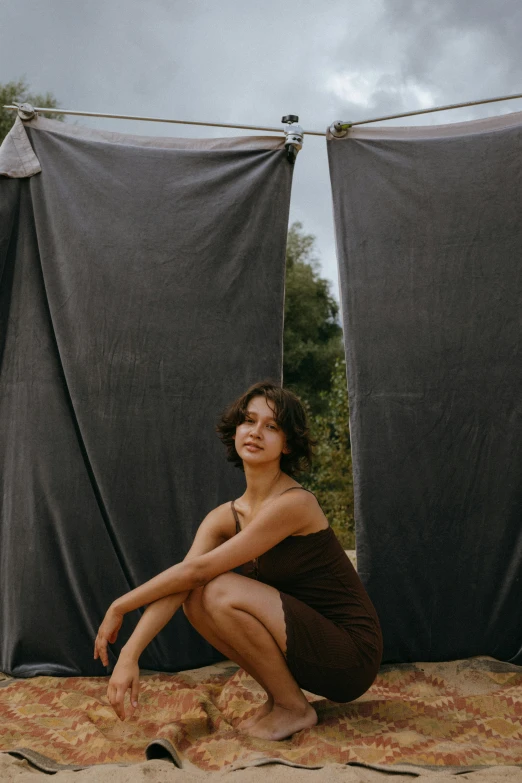 a woman sitting on top of a blanket on top of a beach, an album cover, by Attila Meszlenyi, unsplash contest winner, renaissance, leaning on door, isabela moner, black and brown, photo booth