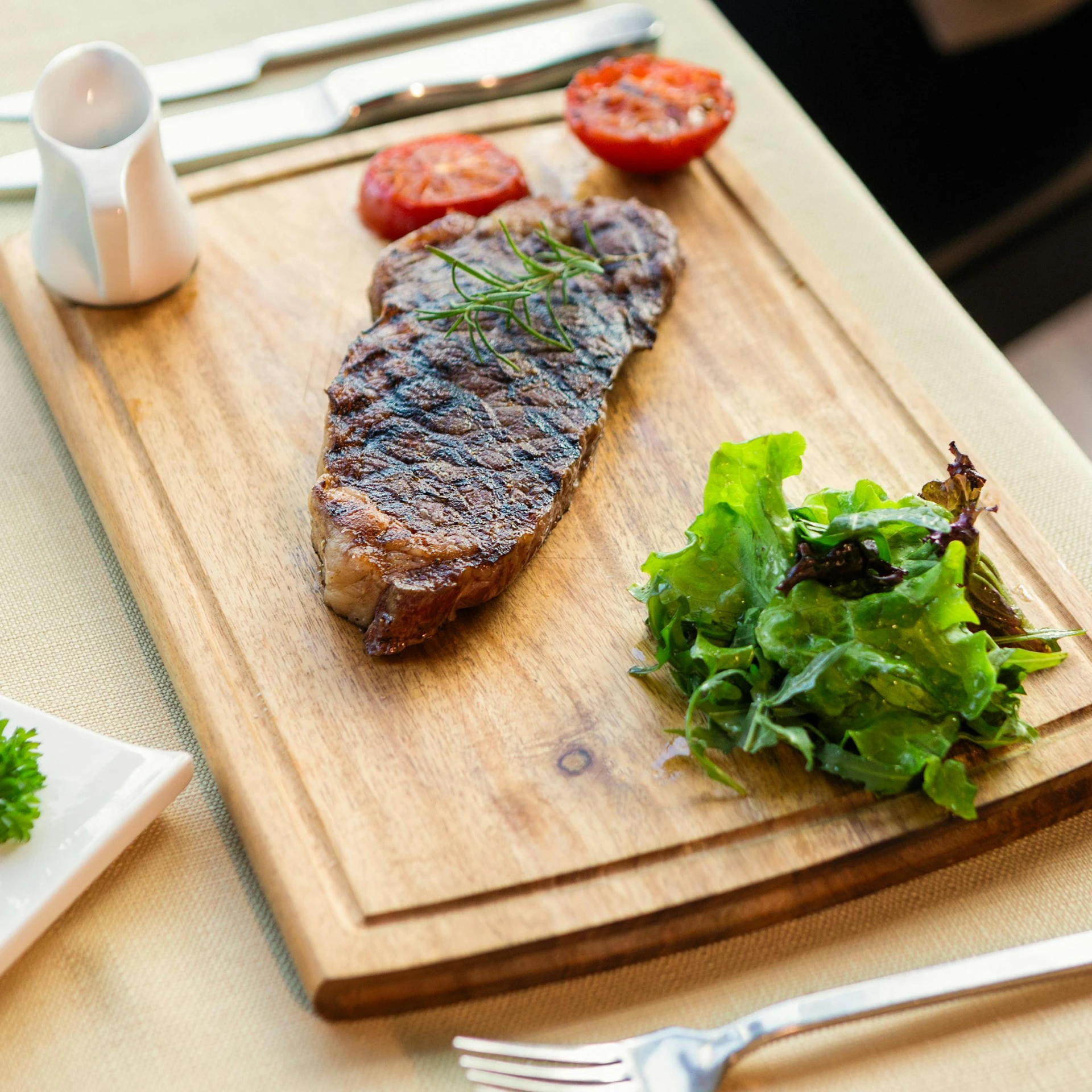 a wooden cutting board topped with meat and vegetables, sitting at table, steak, during the day, restaurant