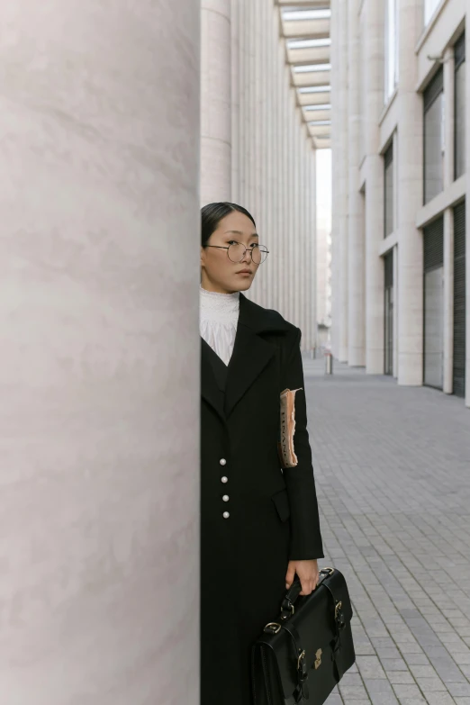 a woman in a black coat holding a black bag, inspired by Wang E, pexels contest winner, architecture in the background, lawyer clothing, girl wearing round glasses, looking around a corner