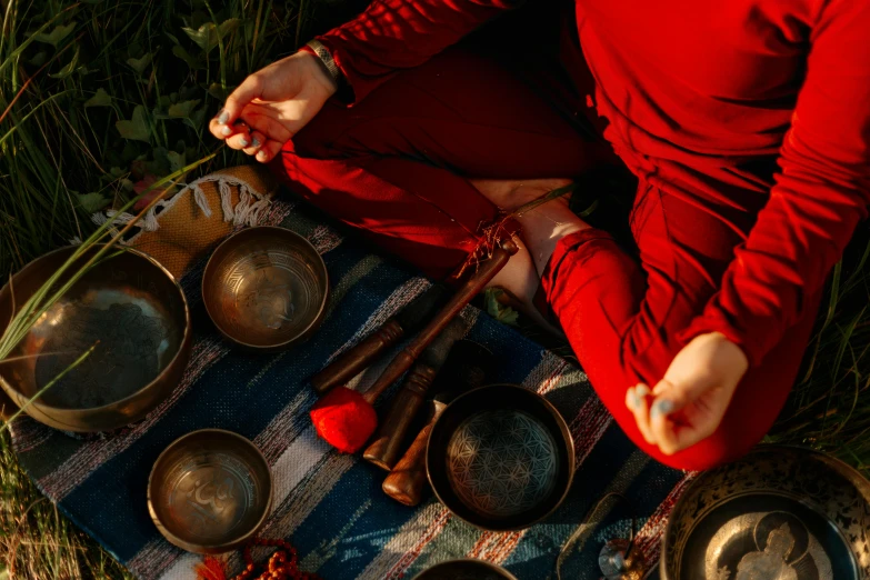 a woman sitting on a blanket in the grass, an album cover, trending on pexels, hurufiyya, in a red dish, alchemical equipment, bells, partially cupping her hands