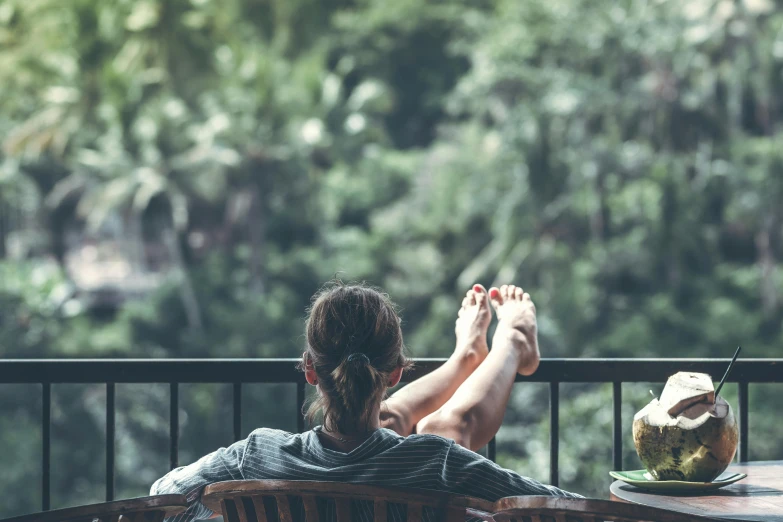 a woman sitting on top of a wooden chair next to a table, pexels contest winner, on a balcony, lush and green, relaxing on the couch, holiday season