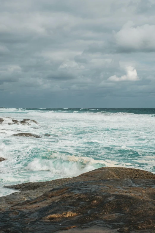 a man standing on top of a rock next to the ocean, by Peter Churcher, unsplash, violent stormy waters, panorama, south african coast, big overcast