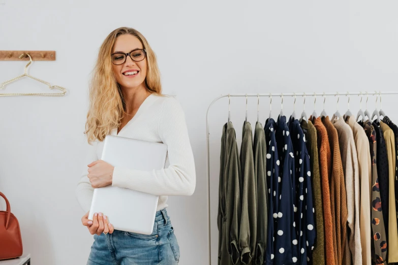 a woman standing in front of a rack of clothes, trending on pexels, figuration libre, holding notebook, with square glasses, white bg, customers