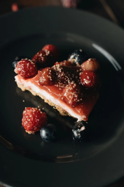 a piece of dessert sitting on top of a black plate, berries, at home