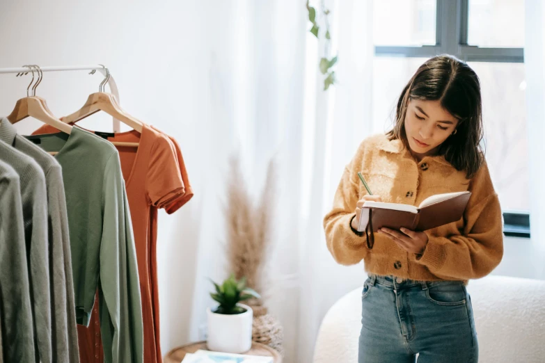 a woman standing in front of a bed reading a book, by Nicolette Macnamara, trending on pexels, clothing design, stood in a supermarket, writing on a clipboard, green and brown clothes