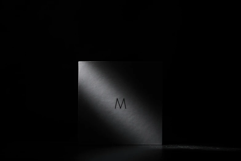 a black box sitting on top of a table, an album cover, by Mathias Kollros, unsplash, black gotic letter m, made of brushed steel, product studio lighting, detailed product shot