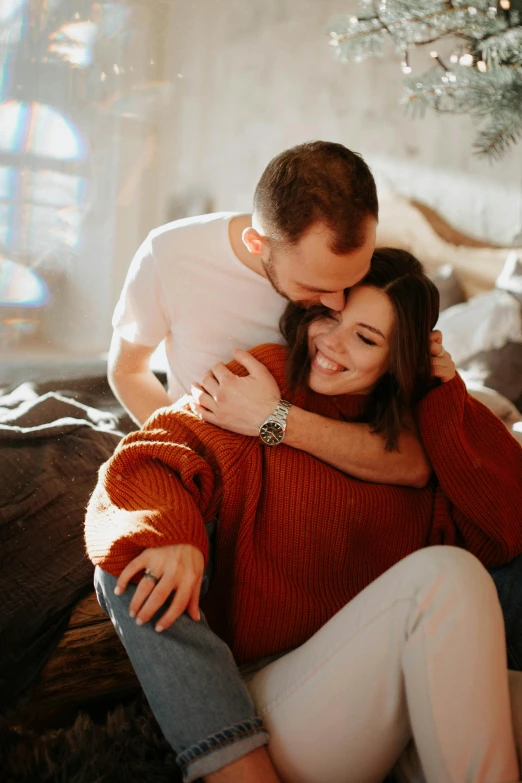 a man and woman sitting on a couch in front of a christmas tree, a picture, pexels contest winner, romanticism, wearing a red turtleneck sweater, loving embrace, natural light in room, brown