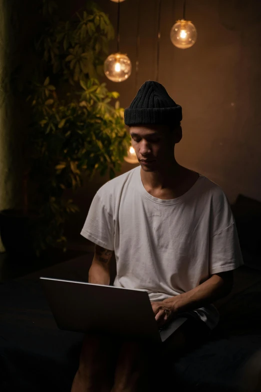 a man sitting on a couch using a laptop, unsplash, realism, standing in a dimly lit room, with black beanie on head, asian human, male with halo